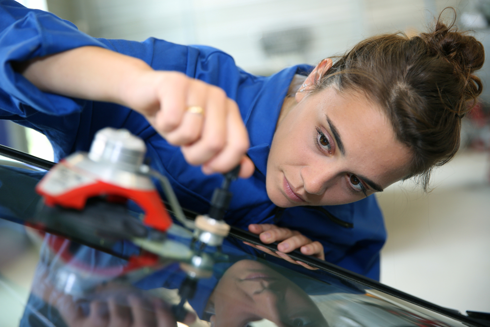 Young student in bodywork changing car windshield