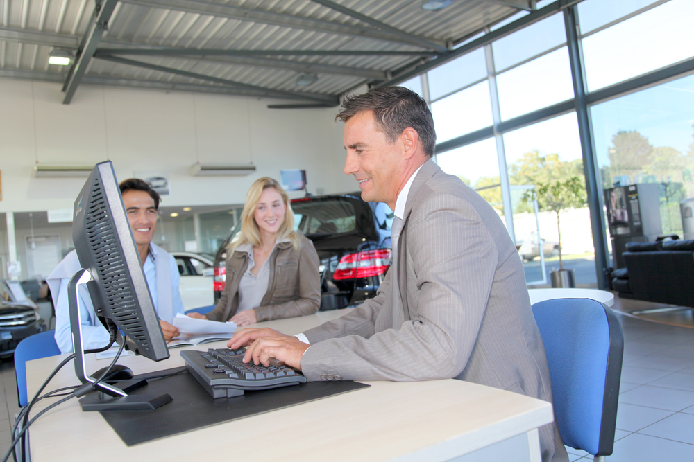 Car seller and couple of buyers signing contract