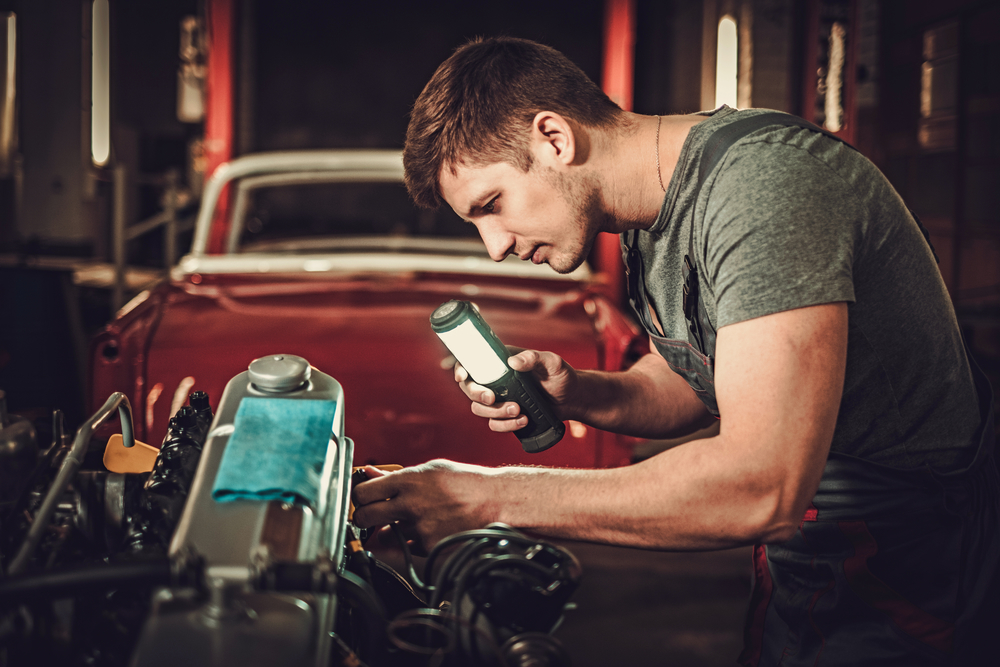 Mechanic working on classic car engine in restoration workshop.