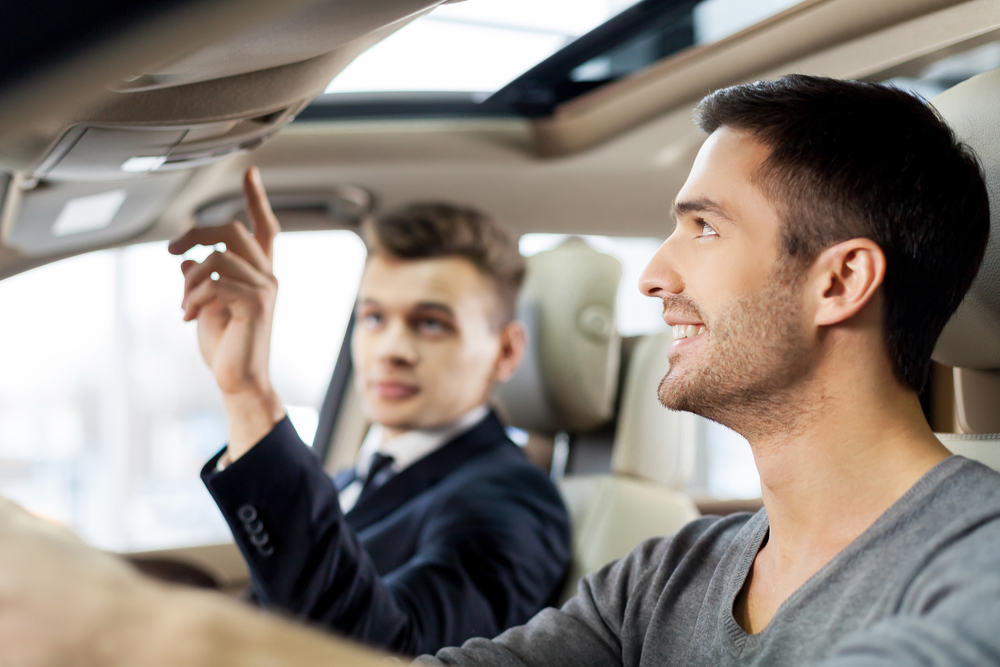 This model comes with added features. Handsome young salesman showing all the car features to the customer