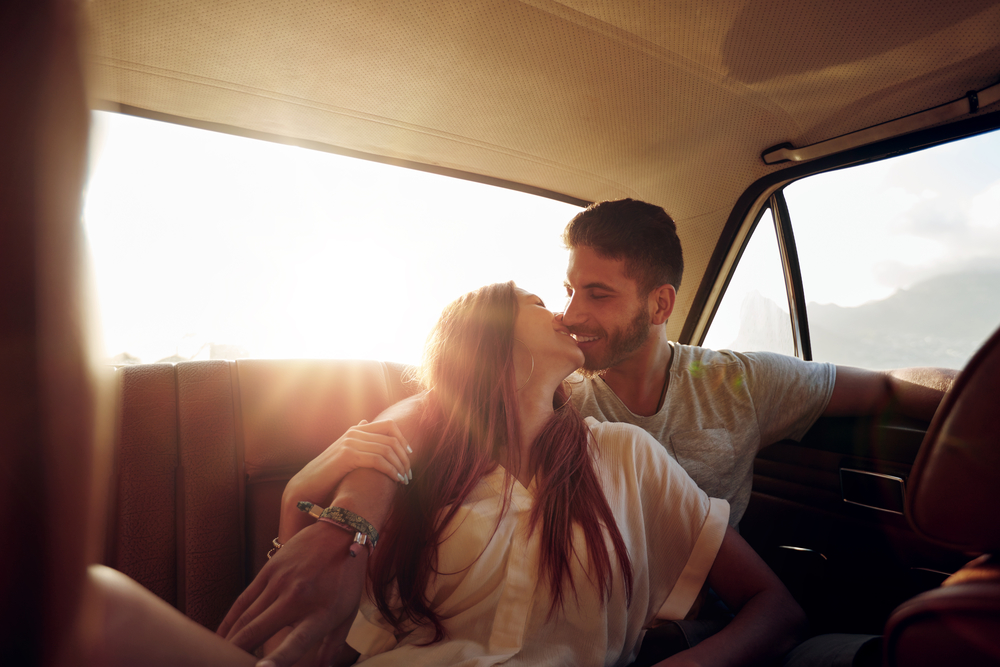 Affectionate young couple sitting in back seat of a car. Young man and woman in rear seat of a vehicle kissing.