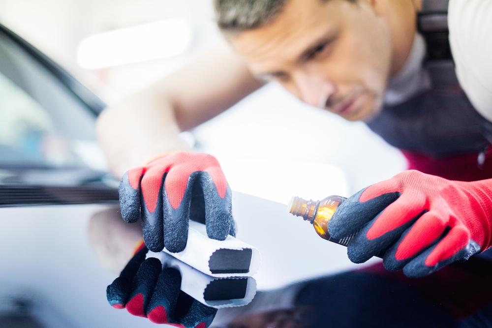 Worker on a car wash applying nano coating on a bonnet