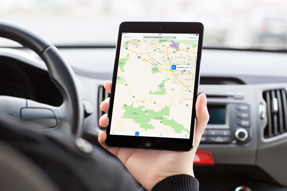 man sitting in the car and holding a mini iPad with Apple Maps o