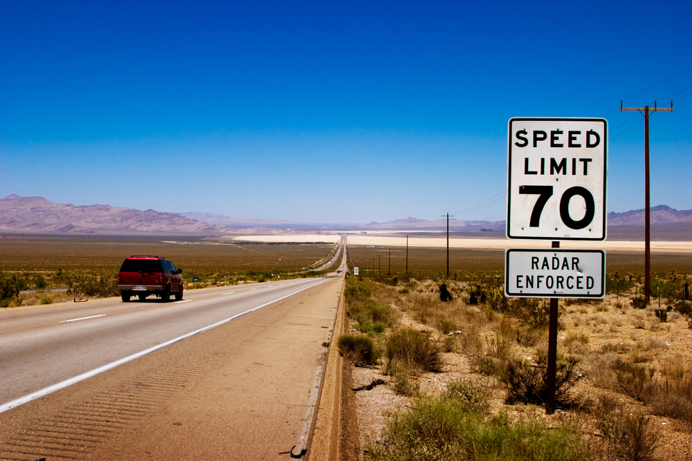 Desert highway to horizon with a speed limit sign on a side.