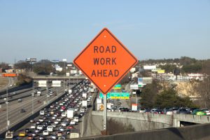 Orange Road Work Ahead Sign showing traffic jam behind in soft focus