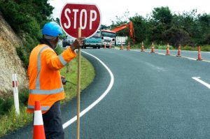 KAITAIA, NZ - 05 DE NOVIEMBRE: Un trabajador de la carretera ralentiza el tráfico con una señal de pare el 05 de noviembre de 2013. El equipo de mantenimiento de carreteras tiene la responsabilidad de las necesidades de mantenimiento diario del sistema de carreteras.