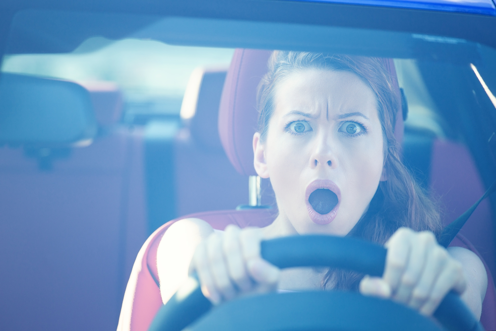 Dear in headlights. Fright face woman driving car, wide open mouth eyes, strongly squeezing wheel, front window view. Negative human face expressions, emotions, reaction. Road trip risk danger concept