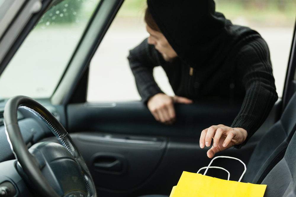 Transportation, crime and ownership concept - thief stealing shopping bag from the car