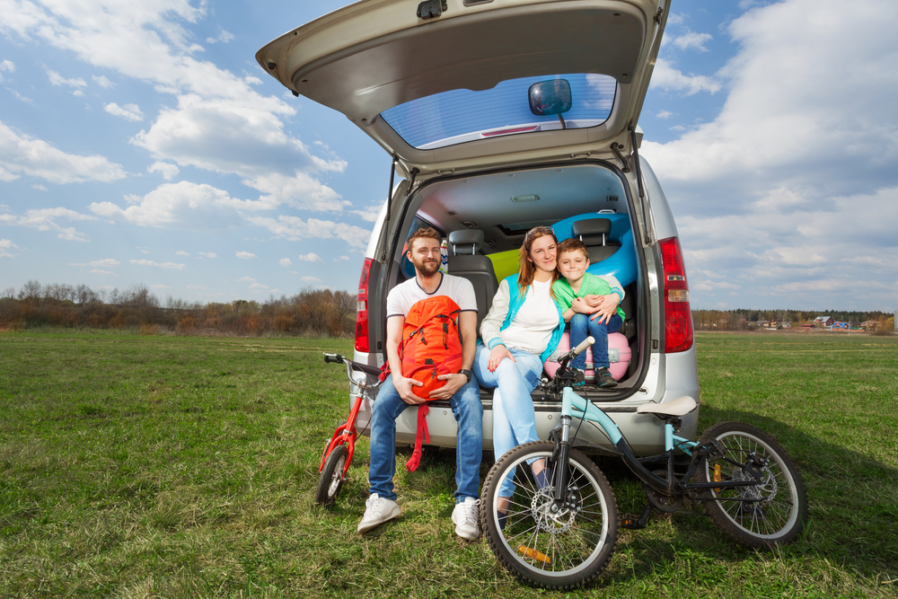 Familia deportista feliz, padres jóvenes y su hijo, sentados en el maletero abierto después de un viaje en coche.