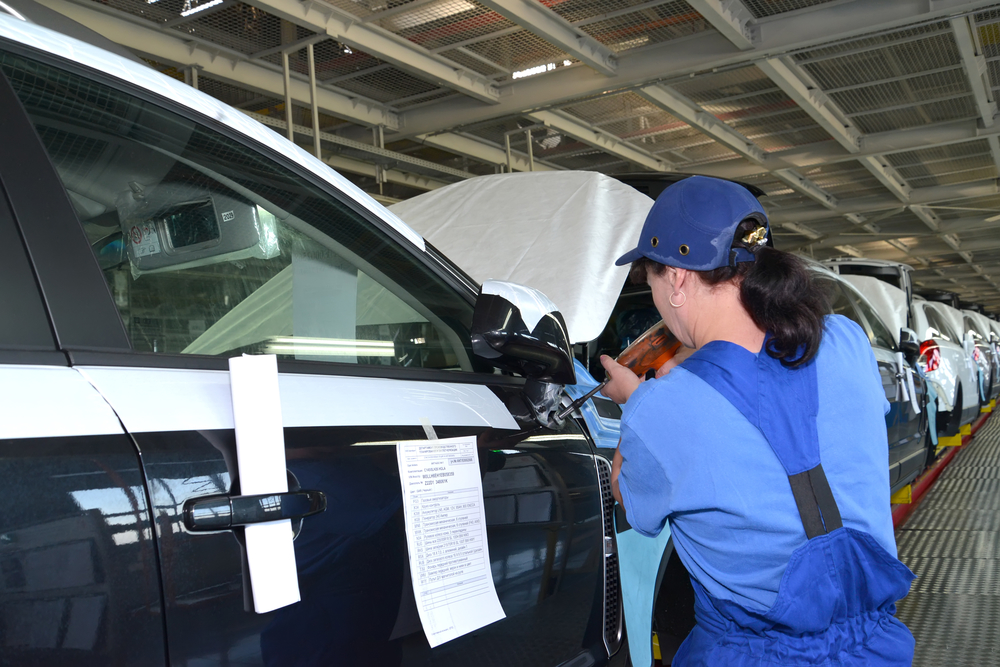 La recolectora fija un espejo en la carrocería de un automóvil con una pistola de tornillos. Transportador de ensamblaje de una planta automotriz.