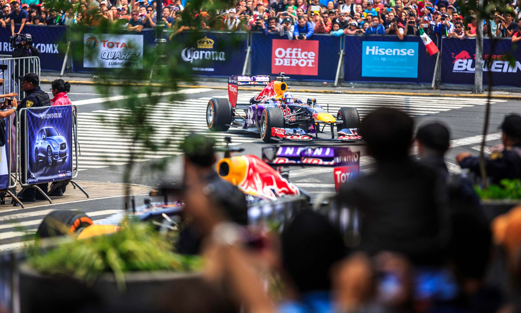 F1 race cars driving around a track with fans cheering.