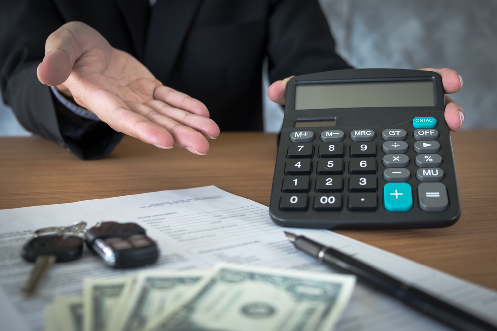 Car salesman holding a key and calculating a price at the dealership office