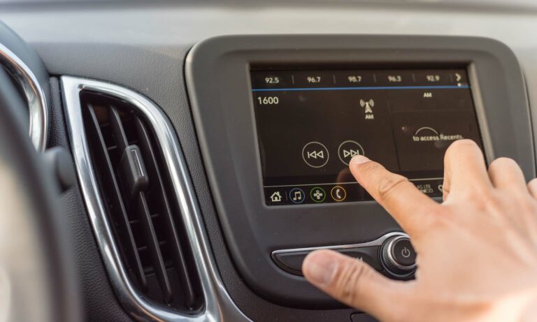 A man's hand reaching for his car's infotainment system on the dashboard.