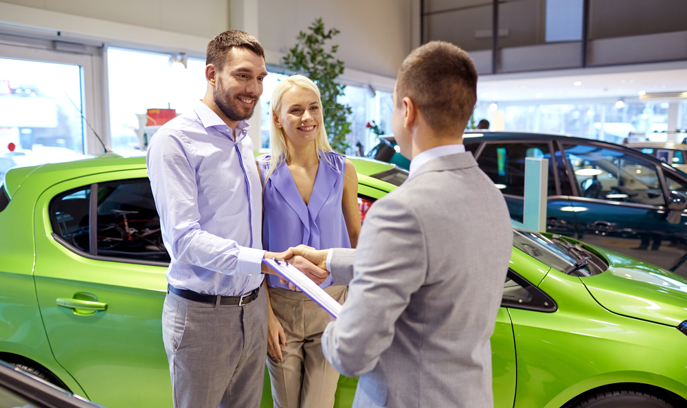 happy couple with car dealer in auto show or salon