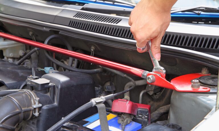 A hand turning a wrench for replacing front strut bar in a car