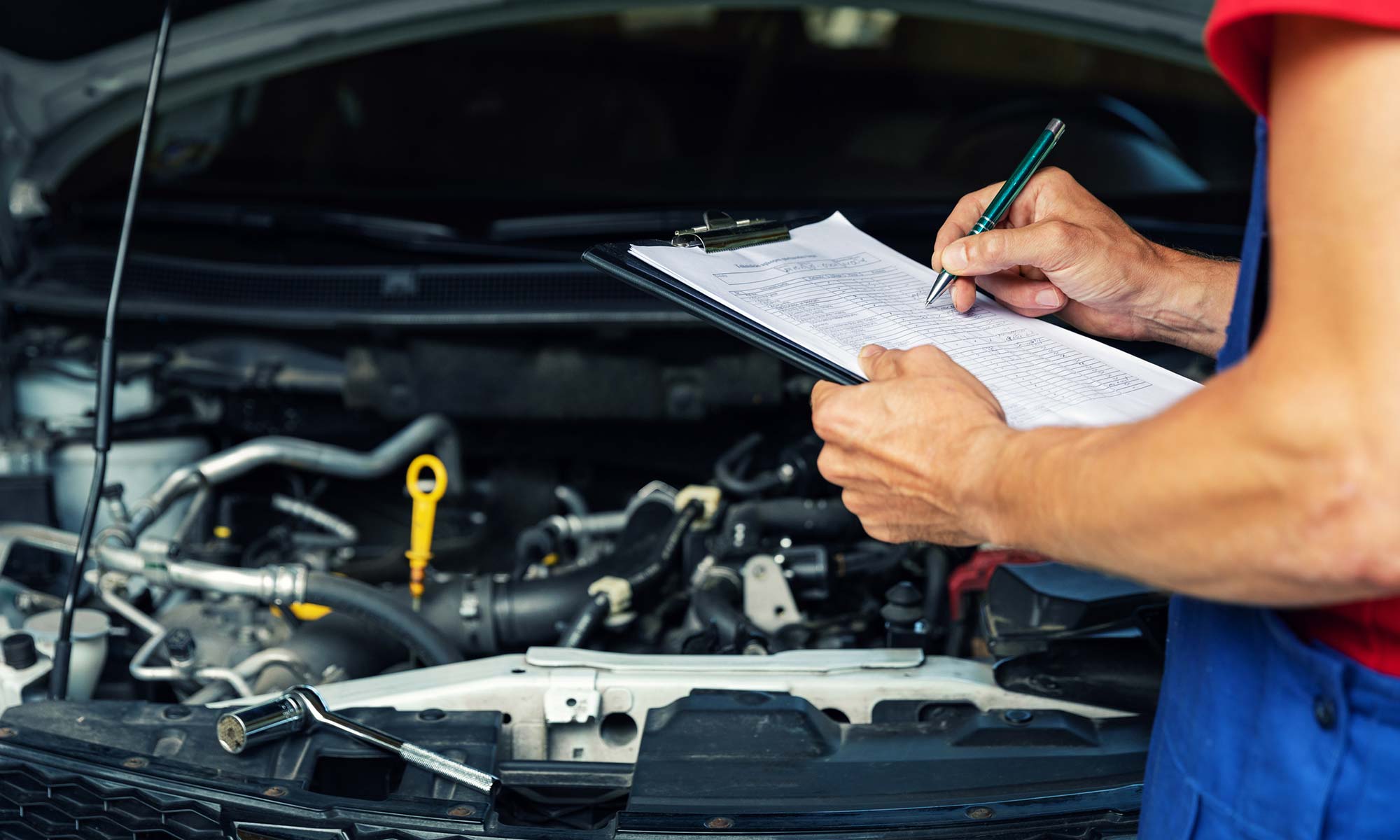 A mechanic writing down notes while inspecting a car's engine during a vehicle recall.