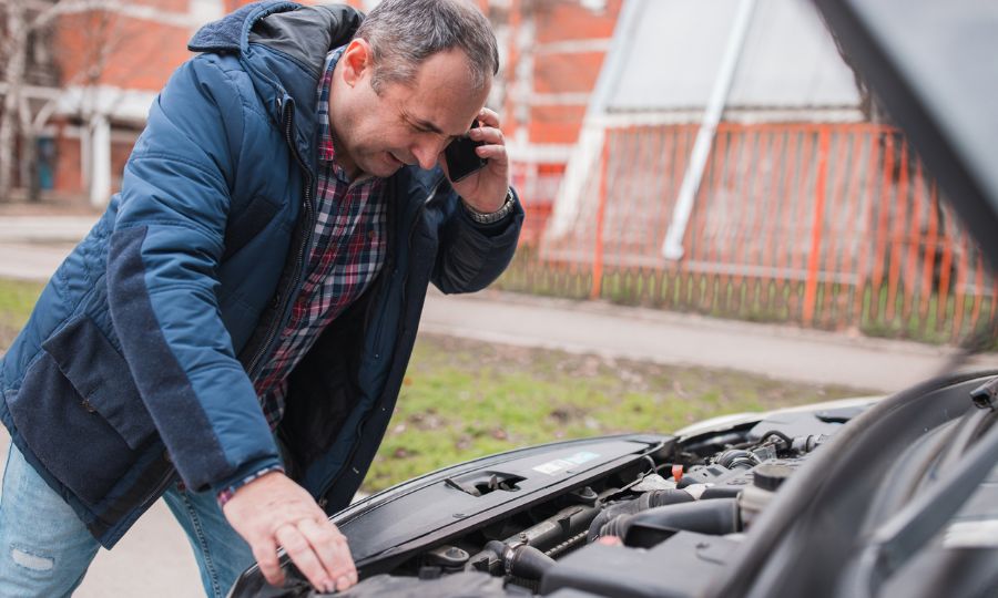 Man calling a mechanic when checking under a hood of his car