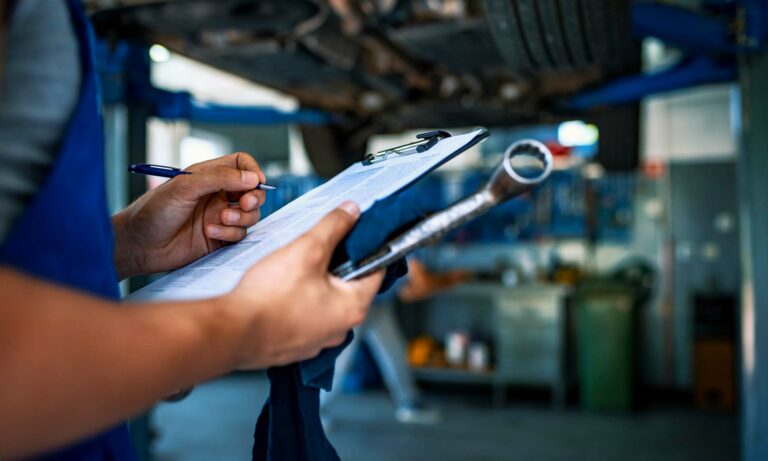 A mechanic checking his clipboard while inspecting vehicle.