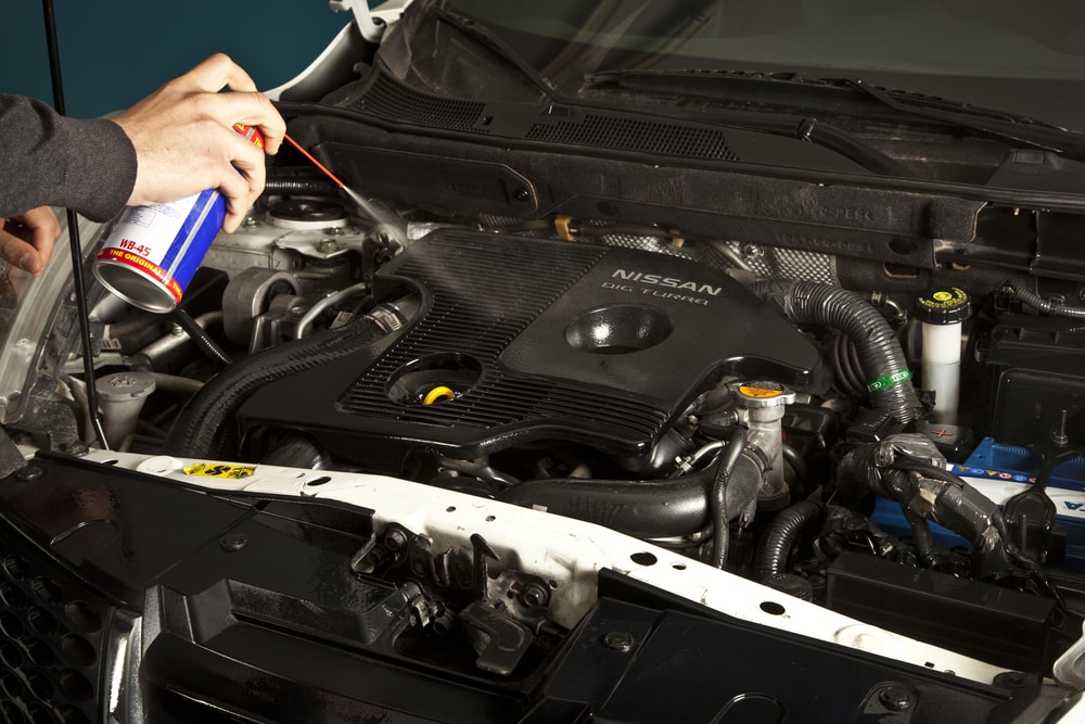 Mecánico reparando un coche en un taller usando WD40 para reducir el ruido.