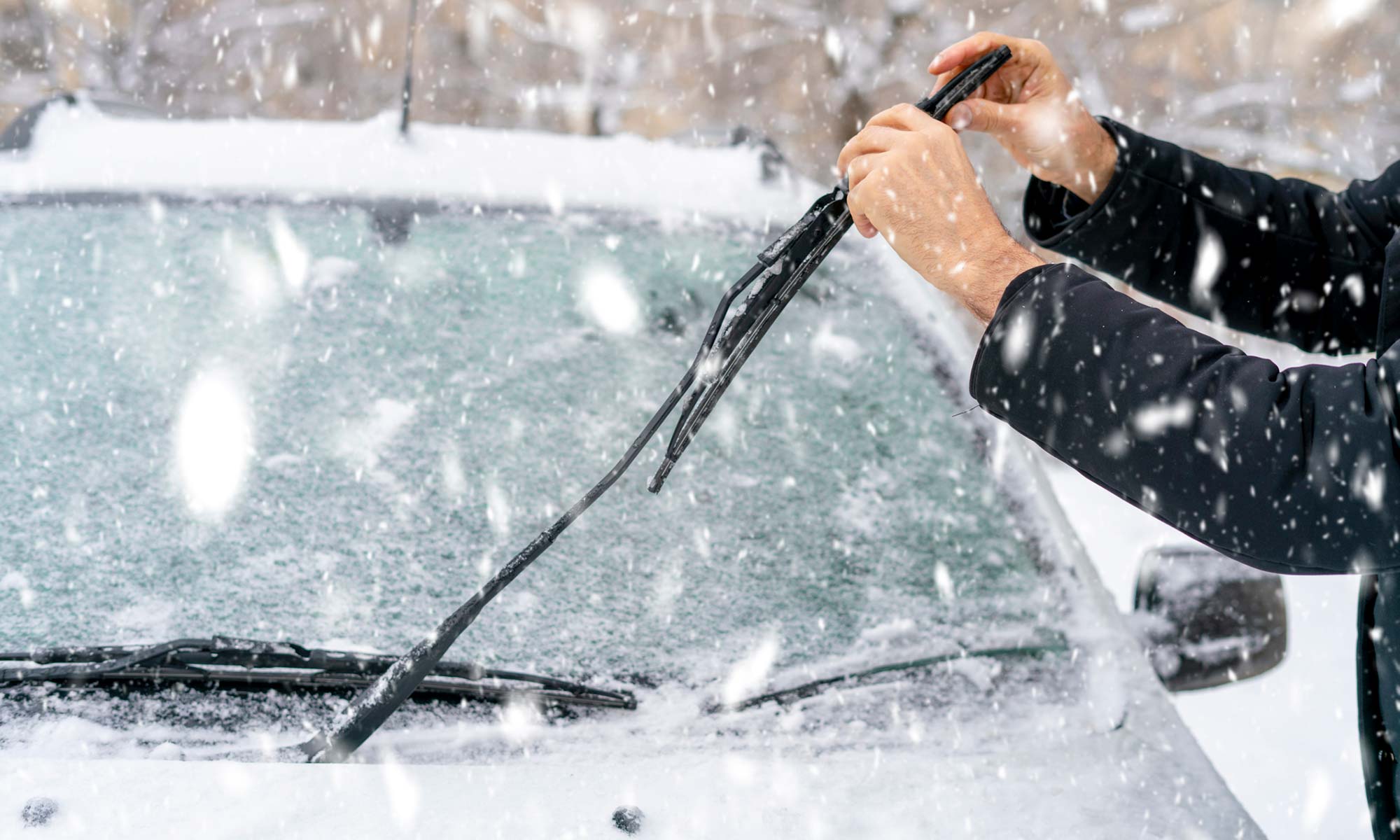Un hombre arreglando las escobillas limpiaparabrisas de su coche en la nieve.