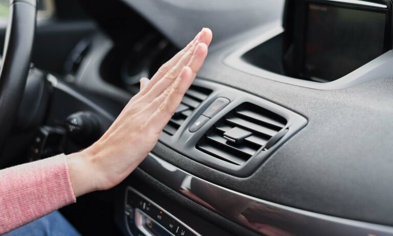 Women's hand held in front of her car's air conditioning vent to make sure it works.