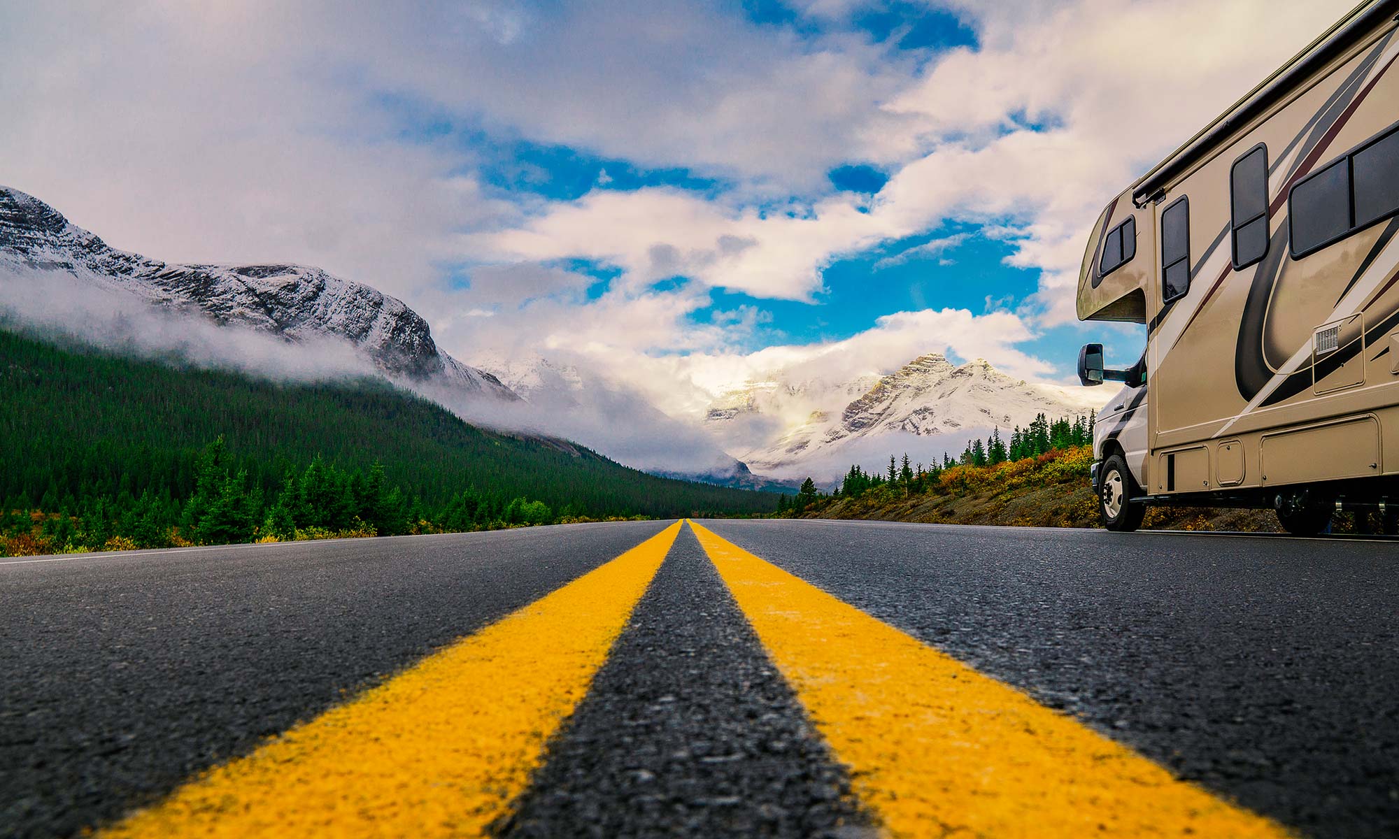 An RV drives down an open road with a scenic mountain view in the background.