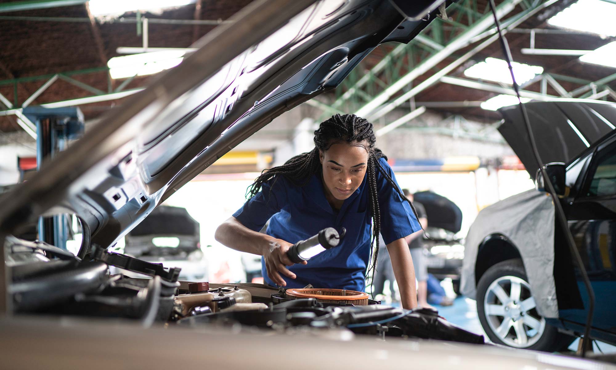 An African American female mechanic inspects the engine of a car.