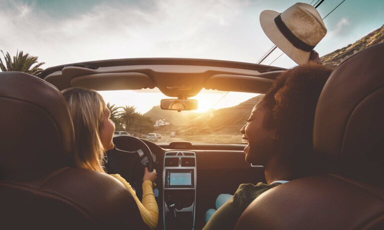 Two female friends having fun and laughing while driving a convertible during sunset with the top down.