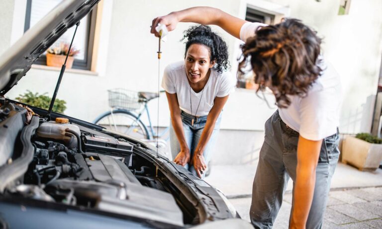 A mother and son checking their car's oil in their driveway.