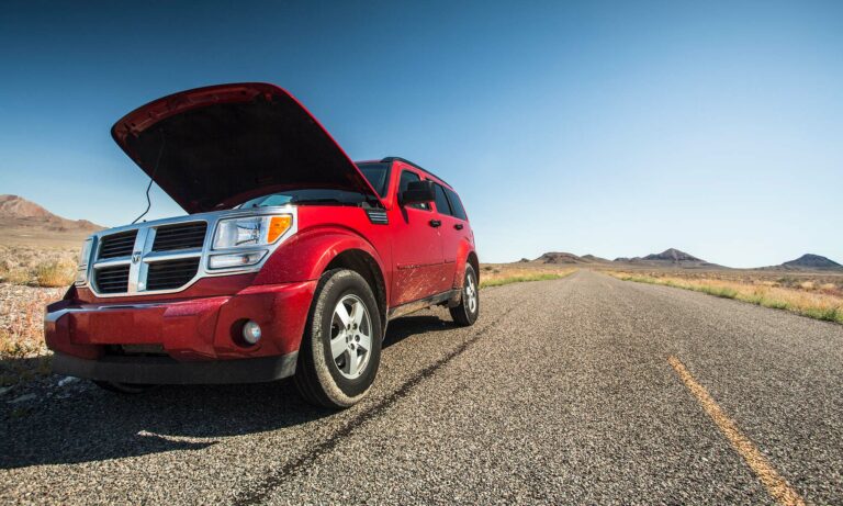 A red Dodge on the side of a desert road with it's hood open.