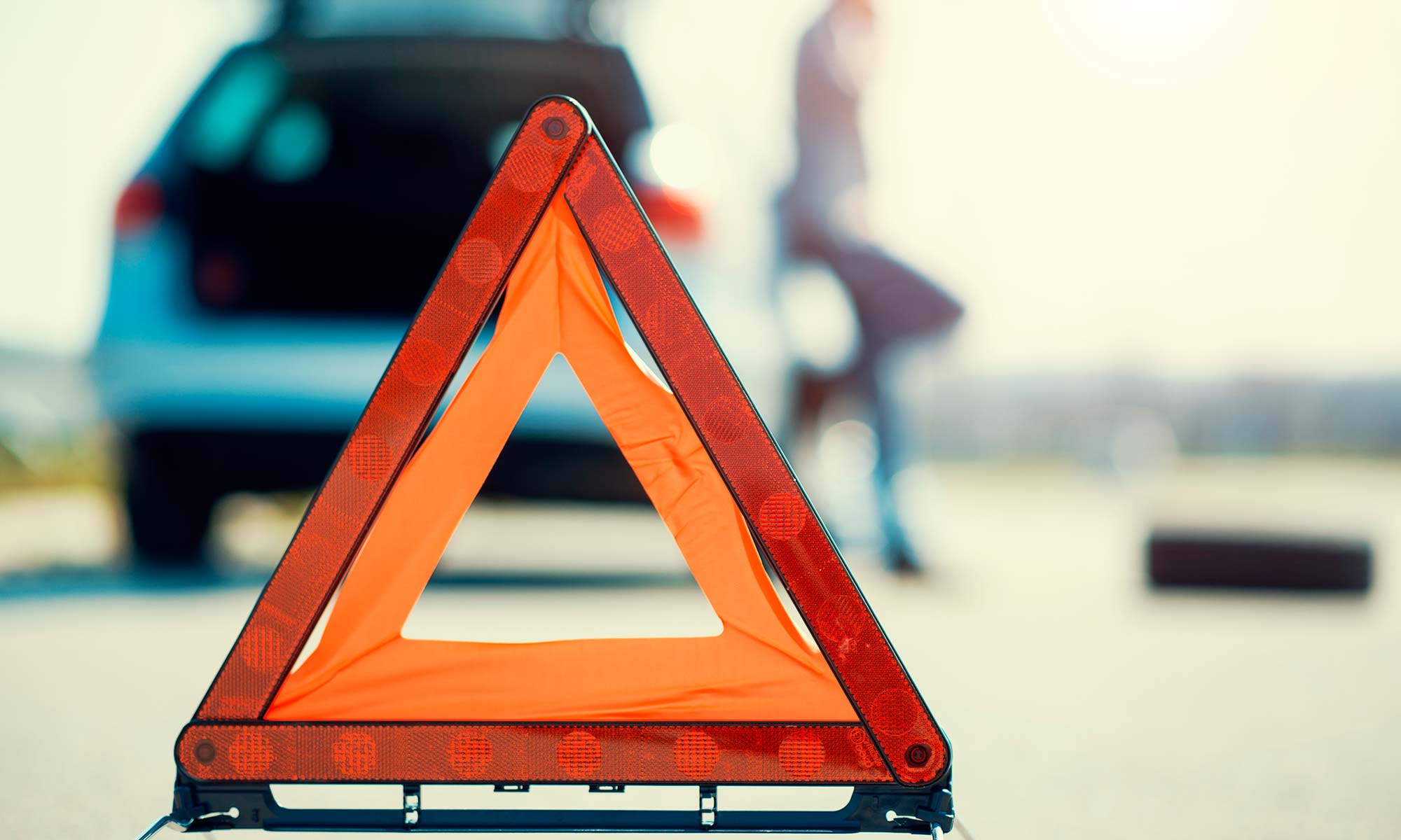 A close up of an orange warning triangle placed on the road in front of a stalled vehicle.