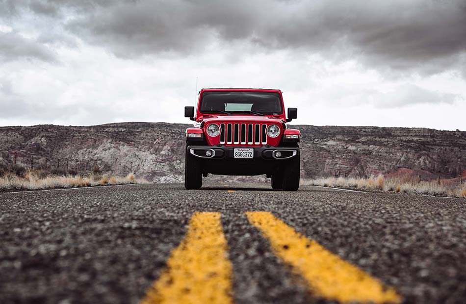 A red Jeep Wrangler driving down a desert road.