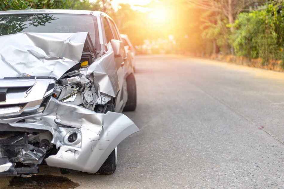 A heavily damaged silver car on the side of the road.
