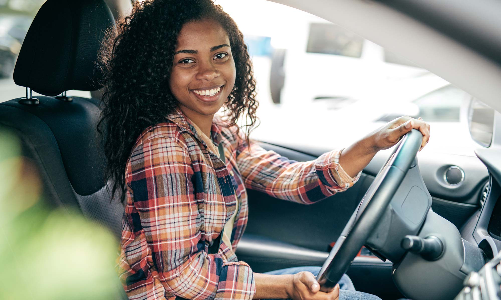 A young woman smiles while in the driver seat of her car.