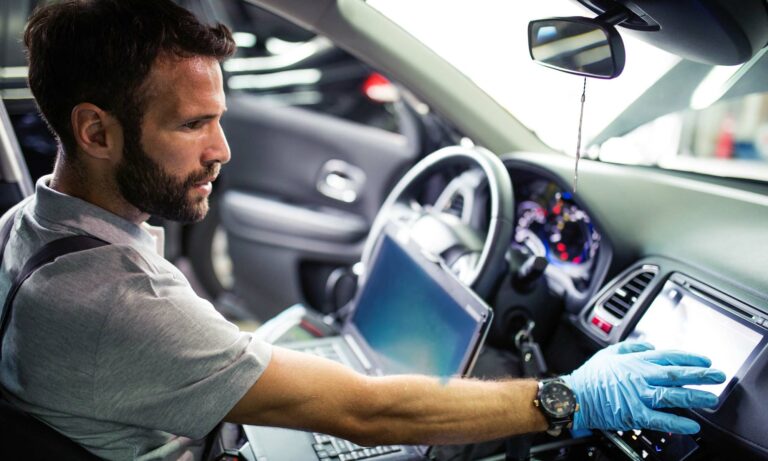 A mechanic using a laptop to diagnose an issue with a vehicle.