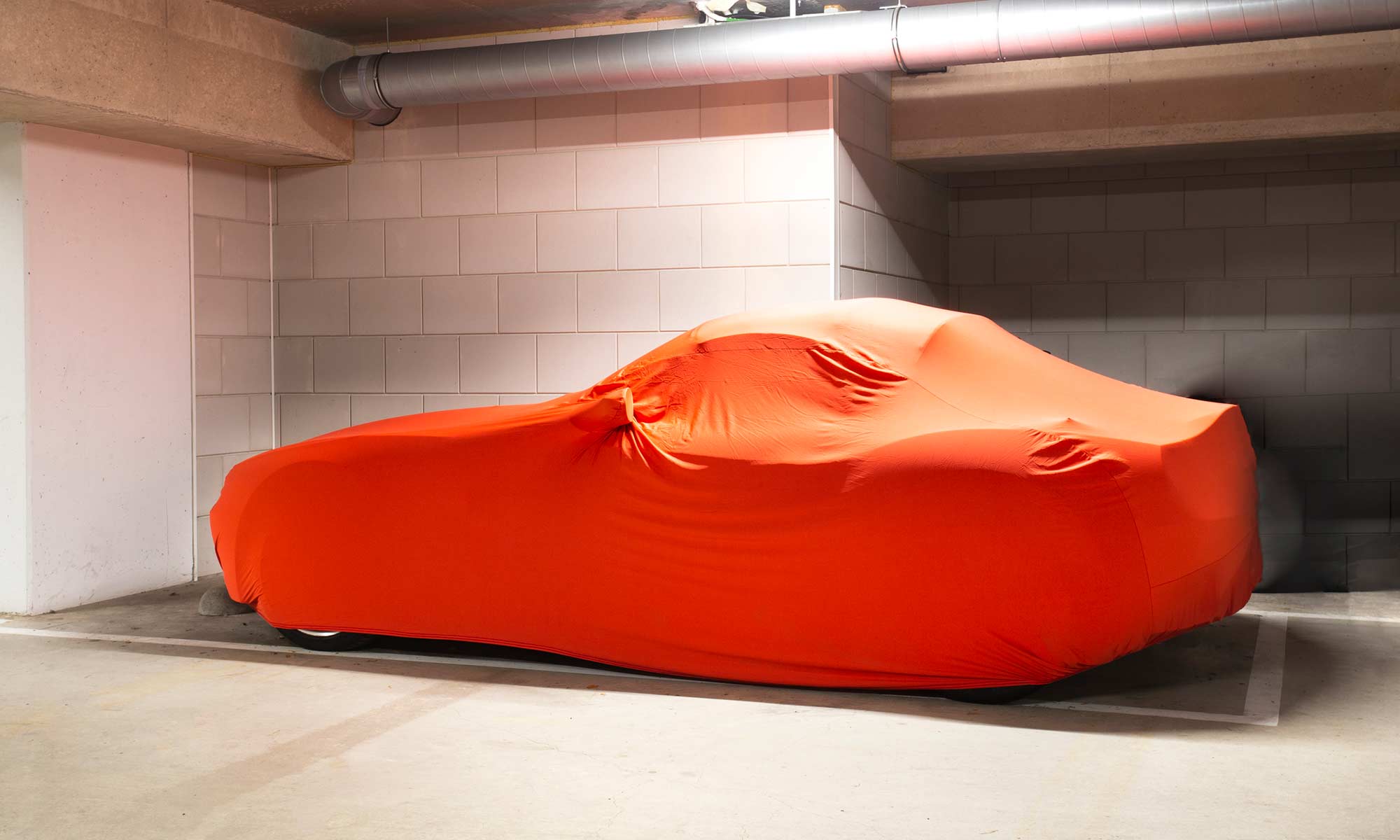 A car parked in a parking garage with a protective car cover on.