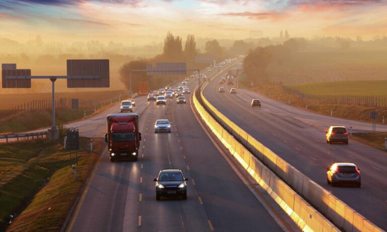 Cars driving down a rural 3-lane highway at dusk