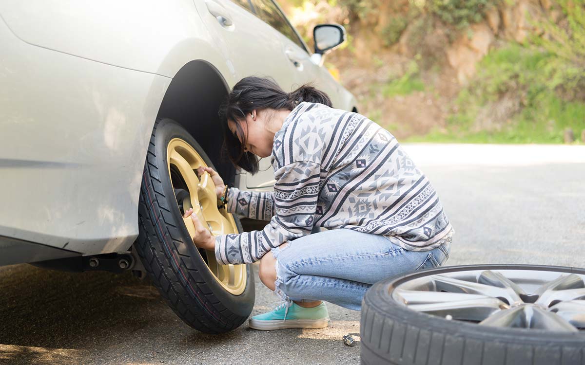 A woman replacing a flat tire.