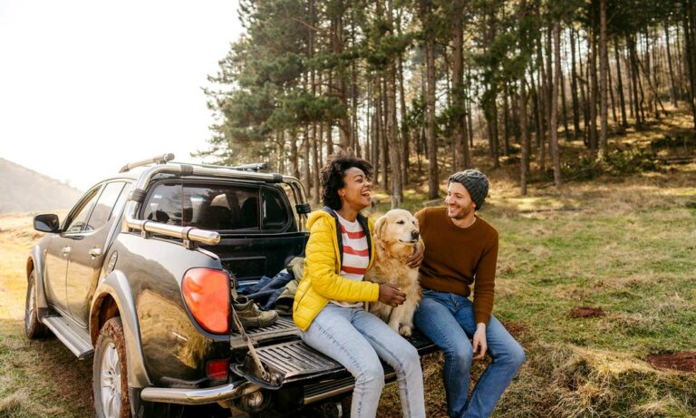 A couple and their dog outside their vehicle.