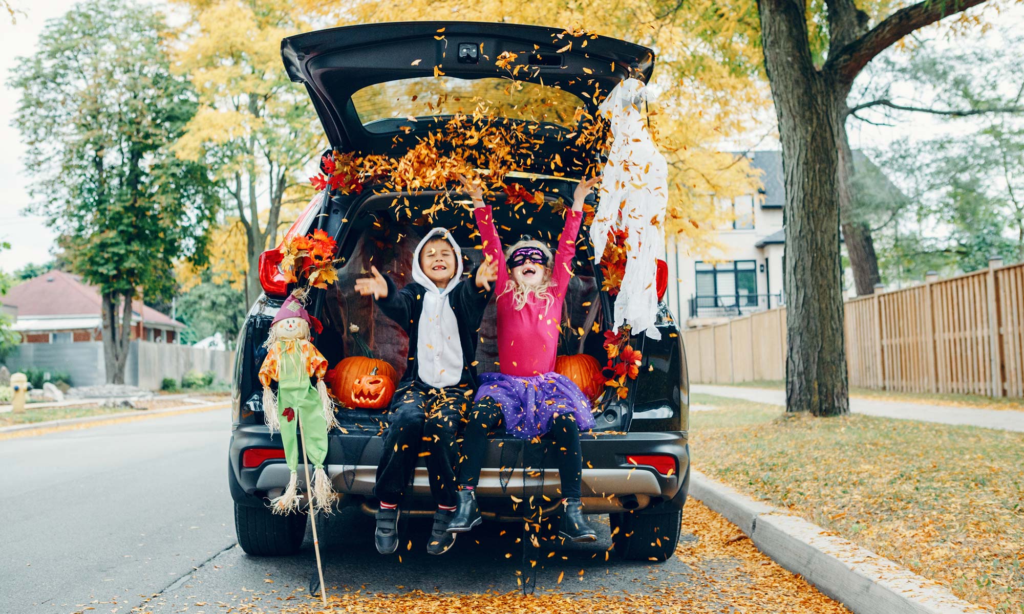 Two young children in Halloween costumes sitting in the trunk of a decorated car.