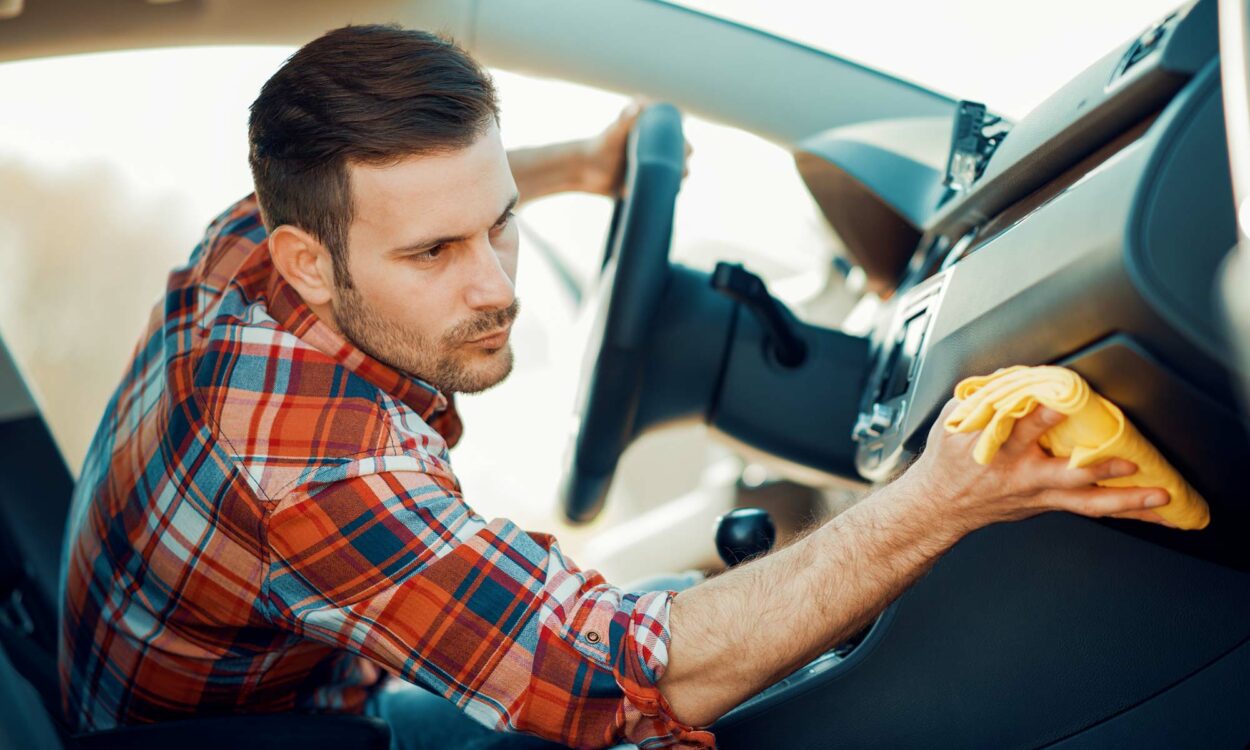 A young man wipes down his car's dashboard.