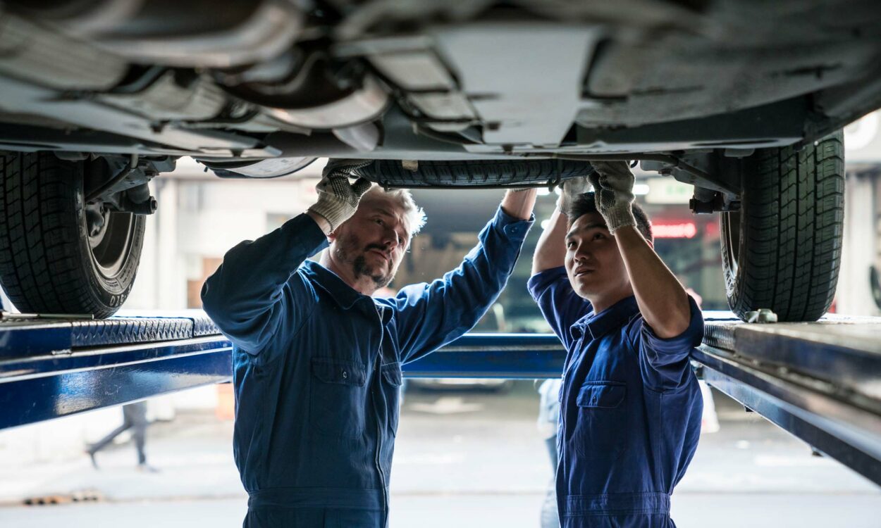 Dos mecánicos de automóviles revisan la transmisión debajo de un vehículo.
