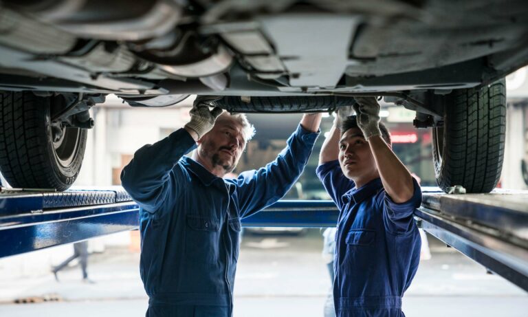 Two auto mechanics checking the drivetrain underneath a vehicle.