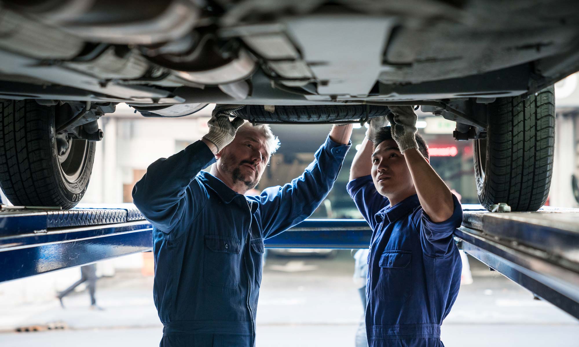 Two auto mechanics checking the drivetrain underneath a vehicle.