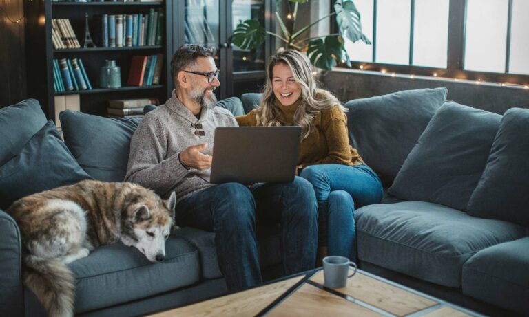 A couple online shopping for a new car on their couch with their husky.