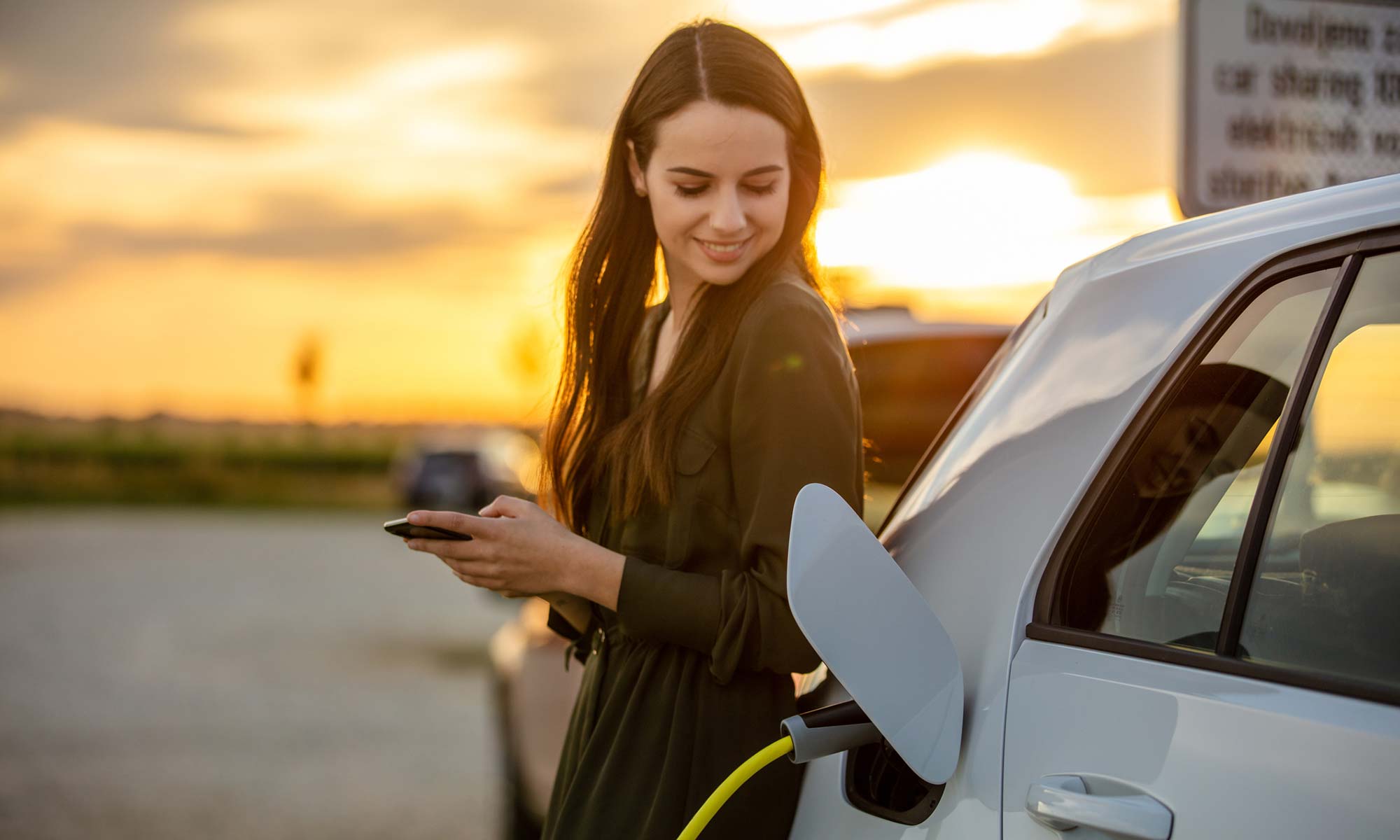 A young woman charging her hybrid vehicle at a charging station.