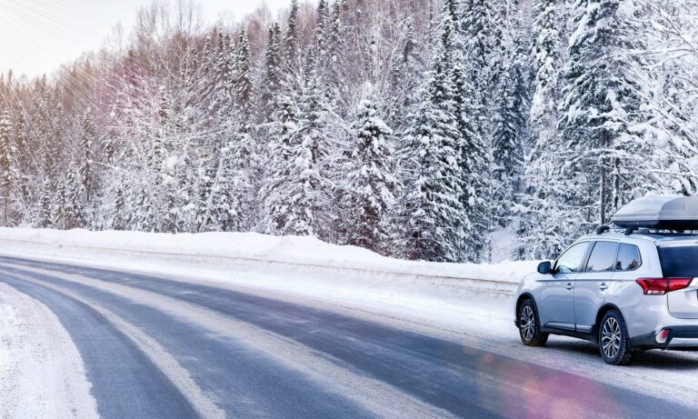 A grey SUV driving down a snow covered forest road.