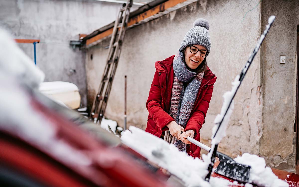 A young woman clears of snow from her car