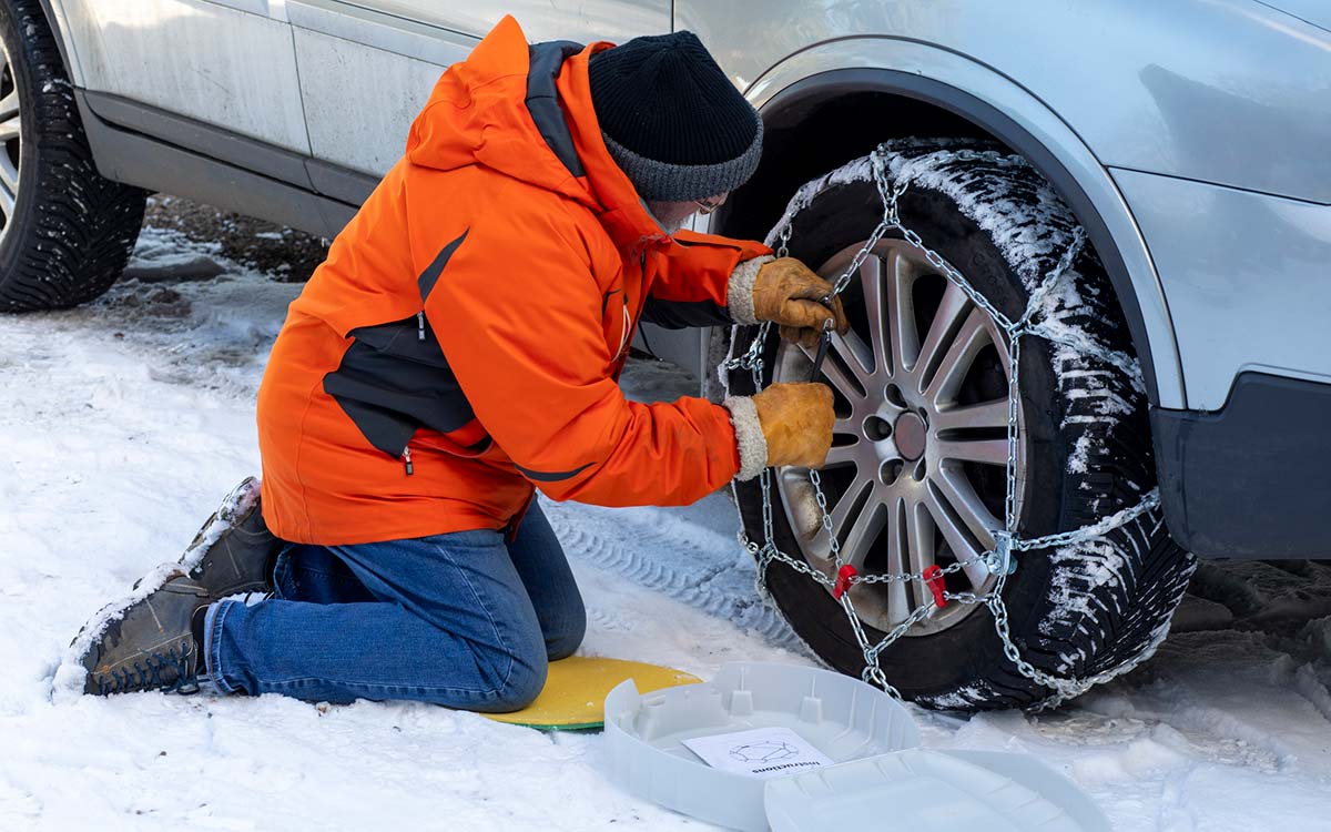 A man placing a tire chain on his tire.