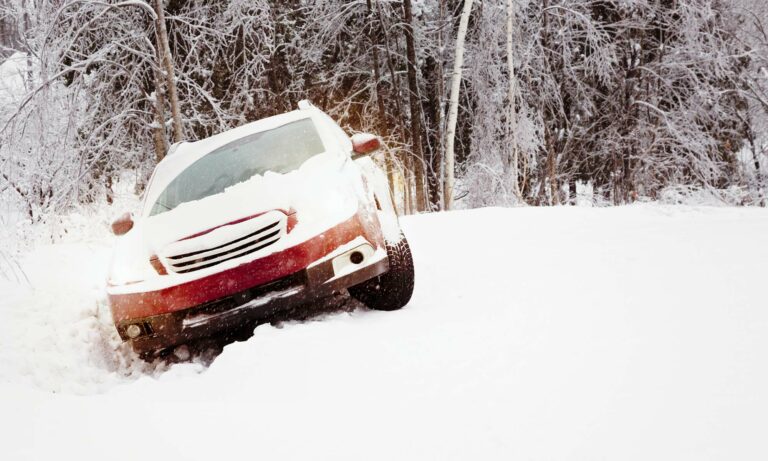 A red car is stuck in a snowbank on the side of the road.